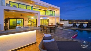 Ein modernes, zweistöckiges Haus mit Pool, Sitzgelegenheiten im Freien und einer Bar.