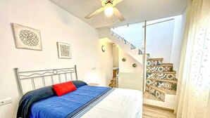 Ein Schlafzimmer mit einem Bett, einem Deckenventilator, einer Treppe mit gemusterten Fliesen und zwei an der Wand befestigten Uhren.