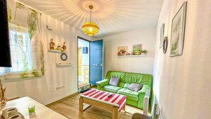 Ein Wohnzimmer mit einem grünen Sofa, einem Couchtisch, einem Kaktus und einem Fernseher an der Wand.