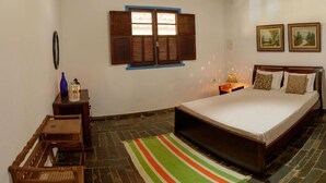 A bedroom with a bed, a nightstand, a lamp, a window with shutters, a wall-mounted mirror, and two framed pictures. - Rustic Farm with Pool Near Curvelo (Corinto)