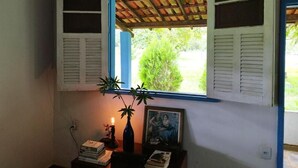 A room with a window, a small table with books and a vase, and a framed picture on the wall. - Rustic Farm with Pool Near Curvelo (Corinto)