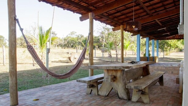 An outdoor covered patio with a wooden table and benches, a hammock, and a view of the surrounding landscape. - Rustic Farm with Pool Near Curvelo (Corinto)