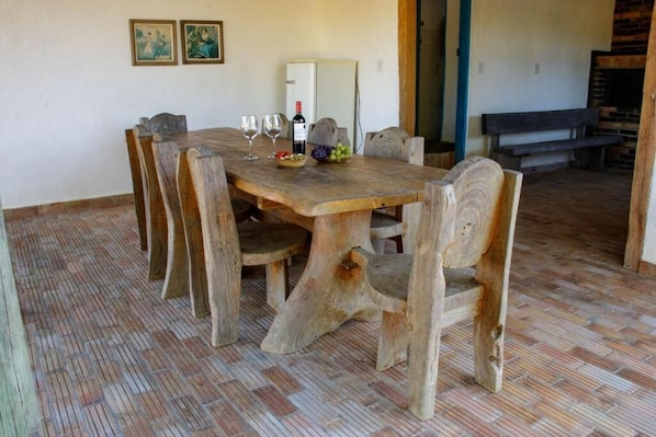 A rustic dining area with a wooden table and chairs, a refrigerator, and a bench in the background.