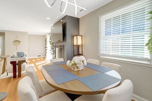 A modern dining area with a round table, white chairs, and a vase of flowers. - 5BR Luxury Home near Washington D.C. with Game Room and Big Back Yard (Alexandria)