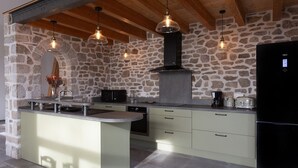 Une cuisine avec un mur en pierre, un îlot central et des luminaires suspendus.