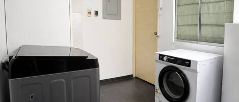 Una sala de lavandería con un electrodoméstico grande de color gris, una lavadora blanca y una puerta de madera.