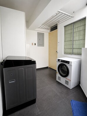 Une buanderie avec un grand appareil électroménager gris, un lave-linge blanc et une porte en bois.