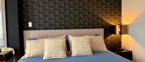 Une chambre d’hôtel avec un lit, une table de chevet, une lampe et un mur orné d’un motif géométrique.