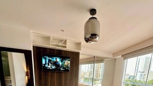 Un dormitorio moderno con una cama grande, un televisor de pantalla plana montado en un panel de madera y vistas de la ciudad a través de amplios ventanales.