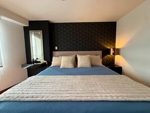 Une chambre à coucher avec un lit, une table de chevet, une lampe et une fenêtre.