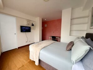 A bedroom with a bed, a television mounted on the wall, a desk, and a chair. - RICARDO PALMA - MIRAFLORES (Lima)