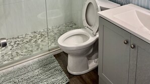 A modern bathroom with a glass shower enclosure, a toilet, and a sink with a towel rack above.