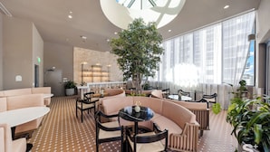 Een moderne lounge met zitgedeelte, een plant in het midden en grote ramen voor natuurlijk licht.