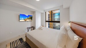 Hotelkamer met een bed, een aan de muur bevestigde televisie, een raam met uitzicht op een gebouw en een houten hoofdeinde.