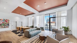 Een moderne woonkamer met een bank, stoelen, een eettafel en een groot raam met uitzicht op de stad.