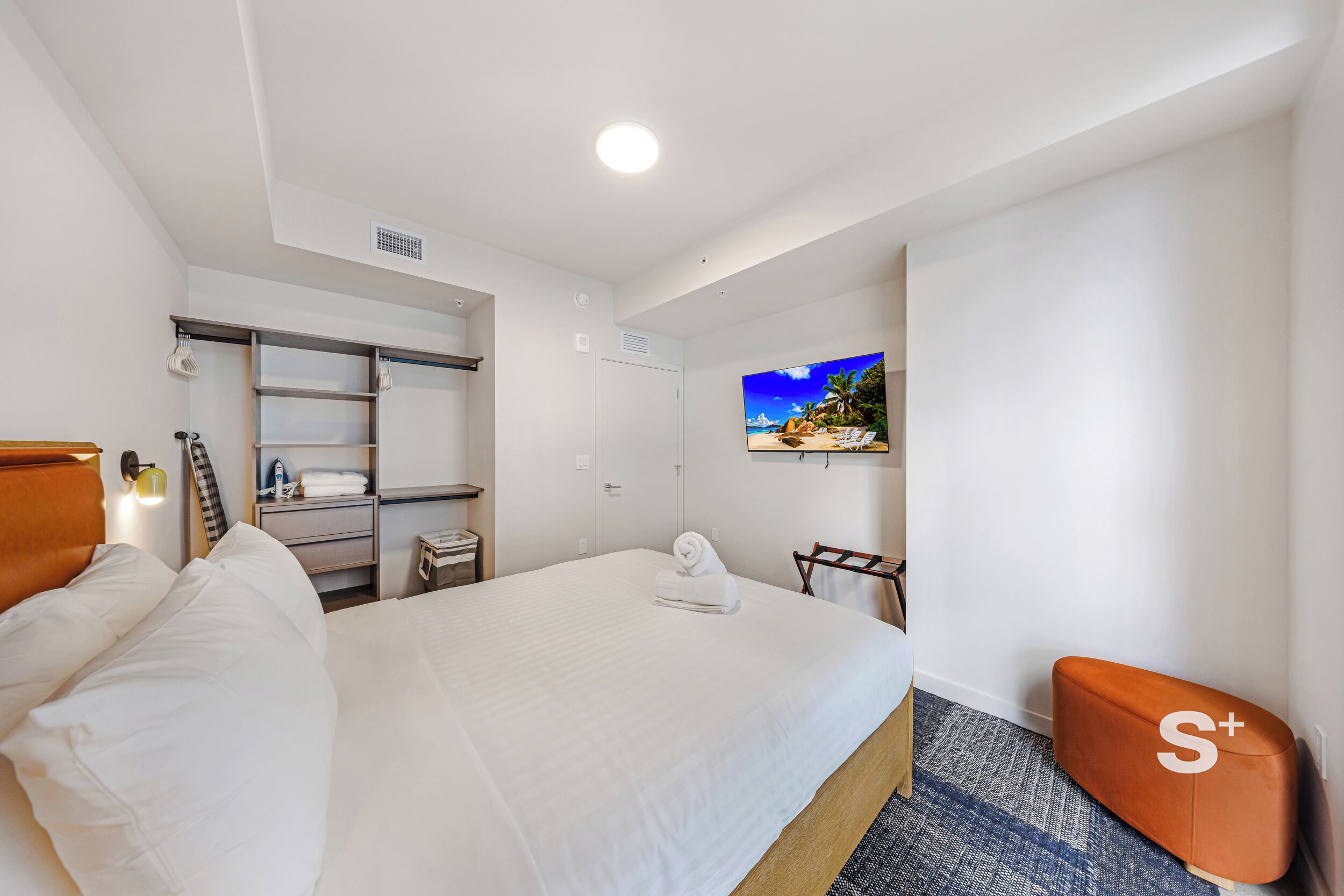Habitación de hotel con una cama grande, televisión montada en la pared, armario y una pequeña zona de estar.