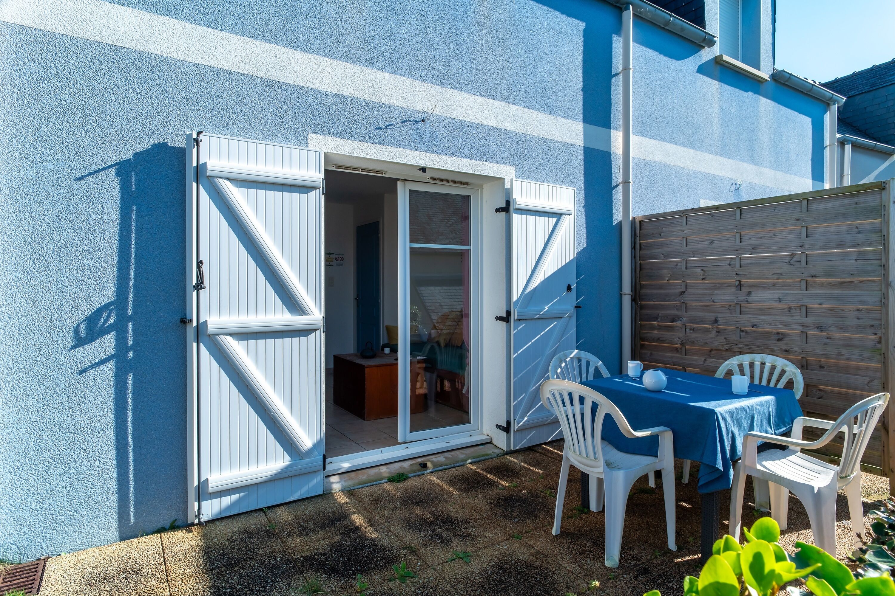 A patio with a table and chairs, a wooden fence, and a sliding glass door leading to an interior space.