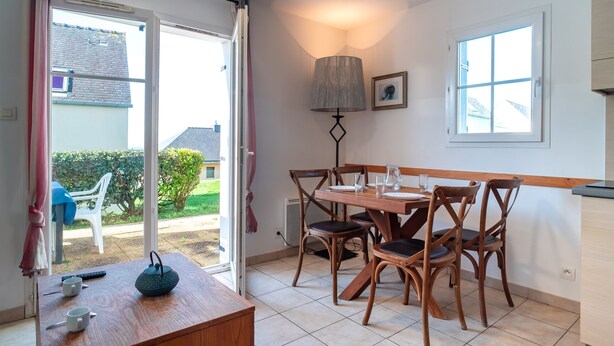 Ein Essbereich mit Tisch für vier Personen, Holzsesseln, einer Lampe und Blick durch eine Glastür nach draußen.
