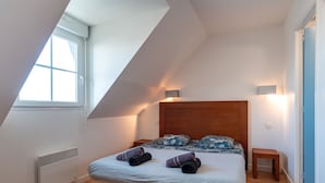 Ein Schlafzimmer mit schrägem Dach, einem Bett mit Holz-Kopfteil, zwei Nachttischen und einem Fenster.