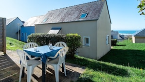 Ein Haus mit einer blauen Tür, einem kleinen Fenster und einem Tisch mit Stühlen davor.