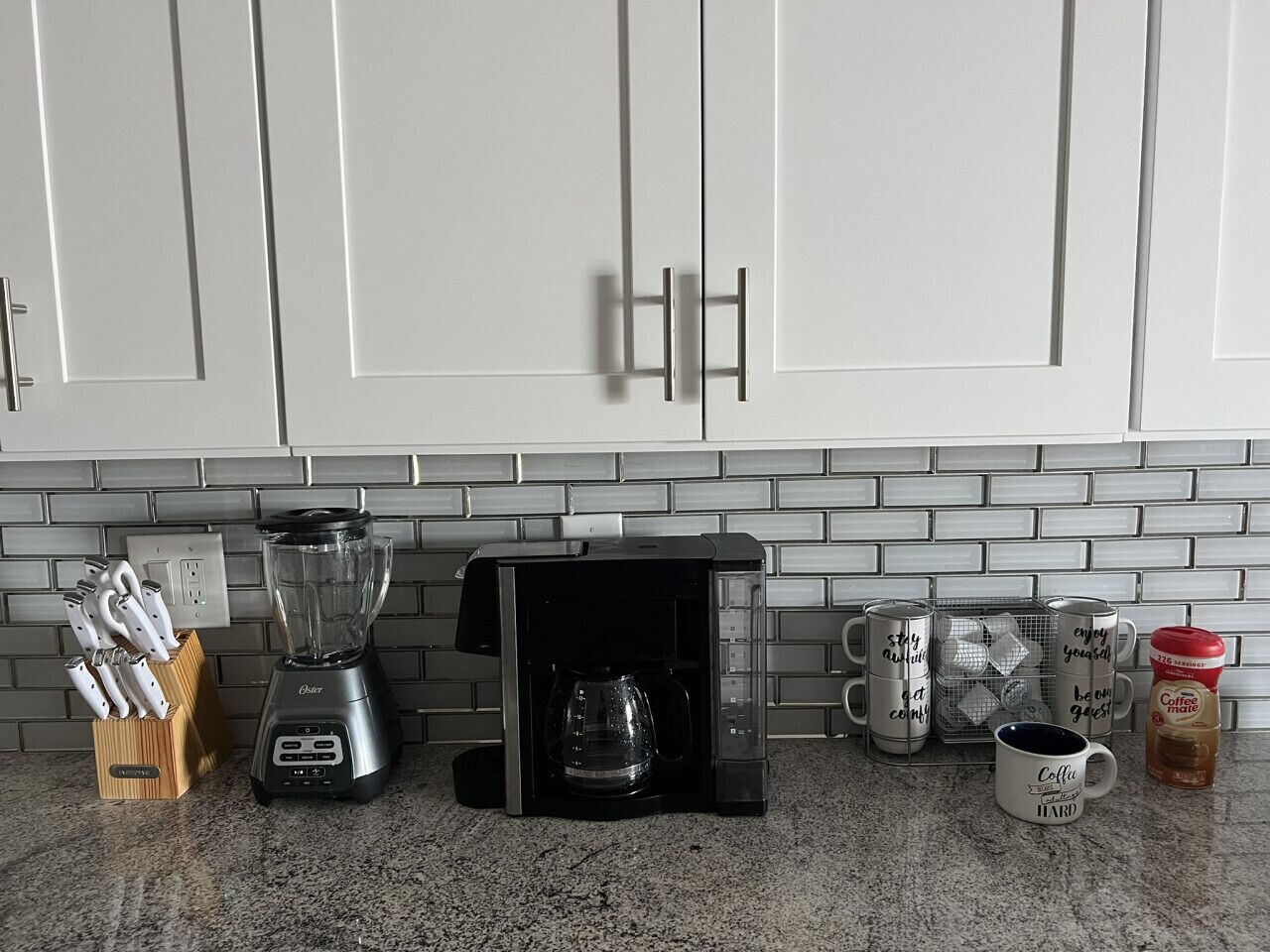 Eine Küche mit weißen Schränken, einer Kaffeemaschine, einem Mixer und einem Messerblock.