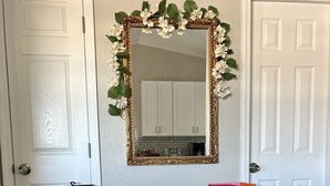 Ein Zimmer mit zwei bunten Stühlen, einem Spiegel mit floralem Rahmen und einer weißen Tür.