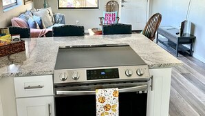 Eine moderne Küche mit Einbauherd, Backofen und Mikrowelle. Es gibt eine Essecke mit einer Couch und Stühlen, einen Deckenventilator und ein an der Wand montiertes Fernsehgerät.
