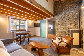 Ein gemütlicher Wohnraum mit Holzbalkendecke, Steinwand und einem Essbereich mit Stühlen und Tisch.
