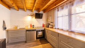 A kitchen with wooden beams, a dishwasher, an oven, and a window with curtains. - L’Écrin des Neiges - Proche Station de Ski (Fontrabiouse)