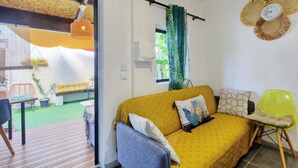 A cozy living room with a yellow sofa, a blue armchair, and a green chair. There is a wooden ceiling and a window with curtains. - Ti Caz la Zac - Parking Privé (La Riviere)