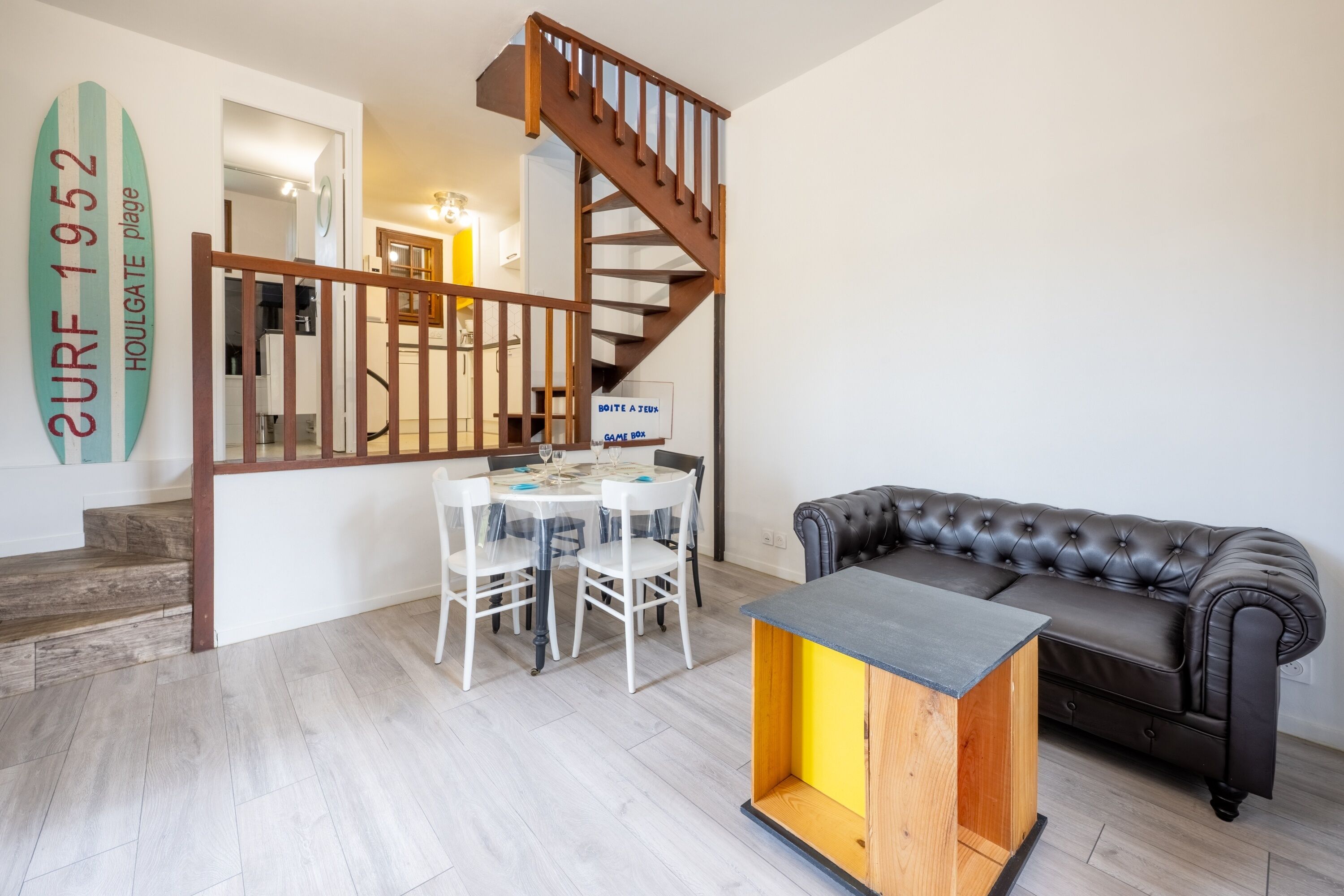 A modern living room with a wooden staircase, a dining table with chairs, a leather sofa, and a coffee table.
