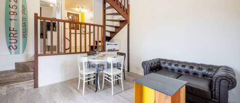 A modern living room with a wooden staircase, a dining table with chairs, a leather sofa, and a coffee table.