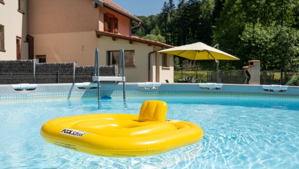 Une piscine avec un flotteur jaune en forme d’anneau, un poste de surveillance pour les sauveteurs et un espace abrité avec un parasol.