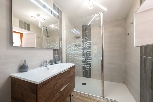 A modern bathroom with a glass shower enclosure, a wooden vanity, and a large mirror.