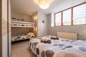 Ein Schlafzimmer mit Etagenbetten, einem Bett mit gemustertem Überwurf, einer Wandleuchte und einem Fenster mit Jalousien.