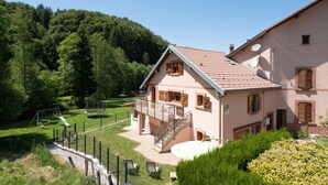 Une maison avec un balcon, un escalier et une cour clôturée équipée d’une balançoire.