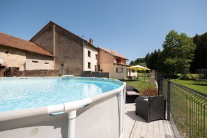 En swimmingpool med en vit kant, en stenmur och en byggnad med ett tak täckt av tegelpannor i bakgrunden.