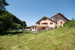 Une maison à deux étages avec un balcon, un petit jardin et une aire de jeux en arrière-plan.
