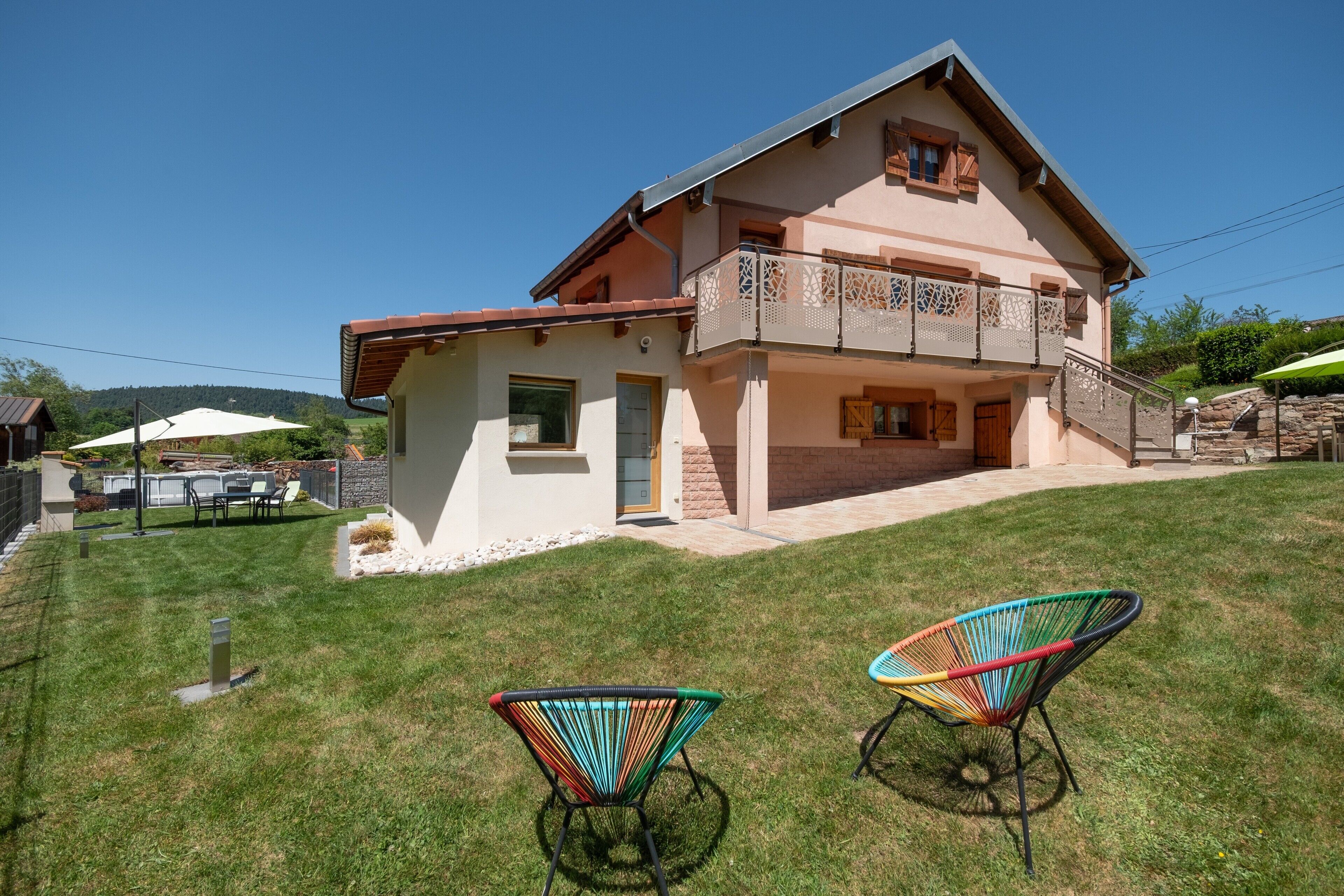 Ein zweistöckiges Haus mit Balkon, einer kleinen Terrasse und zwei bunten Stühlen.