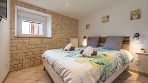 Une chambre avec un mur en pierre, un lit recouvert d’une couvre-lit à motifs floraux, une fenêtre et une table de chevet avec une lampe.