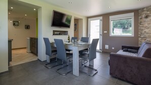 Un espace de salle à manger moderne comprenant une table, des chaises, un téléviseur à écran plat et un mur décoratif en pierre.