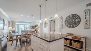 Een moderne keuken met een centraal eiland, hanglampen en een grote wandklok.