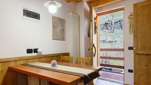 A wooden dining table with a cloth, chairs, a radiator, a wall-mounted light fixture, and a door leading outside. - Maso di Zonadi – Alpine House in the Heart of Val di Rabbi (Rabbi)