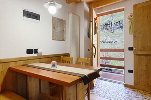 Ein Holzespeisetisch mit Tischdecke, Stühle, ein Heizkörper, eine Wandleuchte und eine Tür, die nach draußen führt.