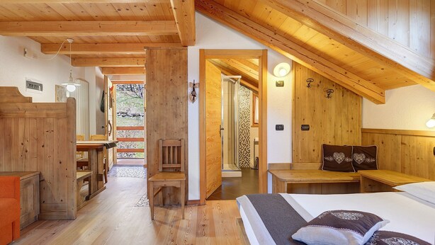 A wooden interior with a bed, a chair, a table, and a bench. - Maso di Zonadi – Alpine House in the Heart of Val di Rabbi (Rabbi)