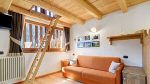 A wooden interior with a sofa, a ladder, a radiator, and a window with curtains. - Maso di Zonadi – Alpine House in the Heart of Val di Rabbi (Rabbi)
