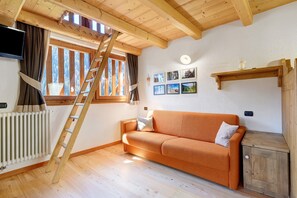 A wooden interior with a sofa, a ladder, a radiator, and a window with curtains. - Maso di Zonadi – Alpine House in the Heart of Val di Rabbi (Rabbi)