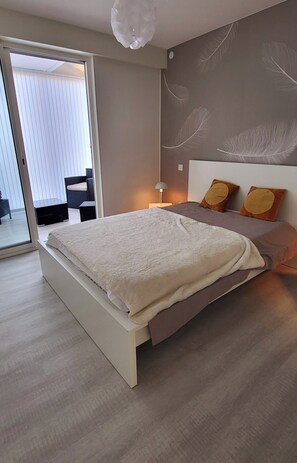 Un dormitorio moderno con una cama grande, un ventanal corredero que da a un balcón y una pared con motivos de plumas.