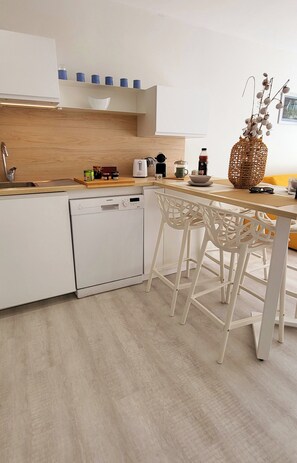 Una cocina moderna con armarios blancos, lavavajillas, encimera de madera y una barra con taburetes blancos.