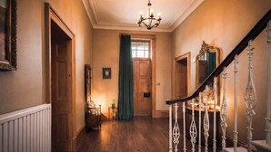 Una imponente escalera con barandillas ornamentales que conduce a un segundo piso, un candelabro colgando del techo y un piso de madera.